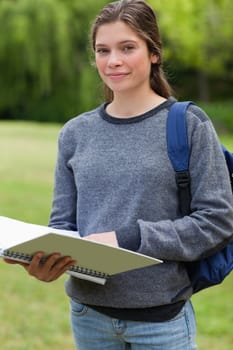 Young girl holding her notebook while carrying her backpack in the countryside