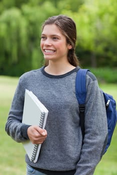 Young girl showing a beaming smile while standing upright and holding a notebook