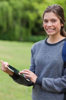 Young smiling girl using her tablet computer while standing upright in a park