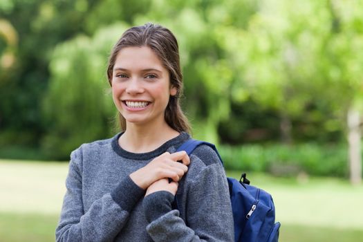 Young smiling girl standing upright in a park while carrying her backpack