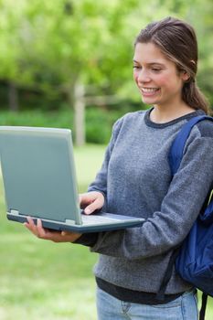 Young student looking at the screen of her laptop while smiling and standing upright