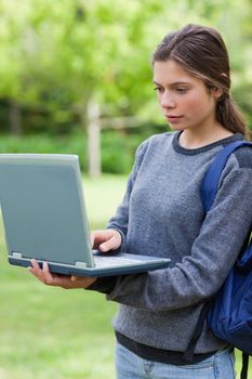 Serious student looking at her laptop while standing upright in the countryside