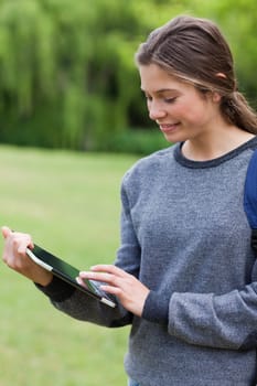 Young happy woman smiling while touching her tablet pc and standing in a park