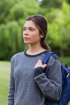 Thoughtful student standing upright in the countryside while carrying her backpack