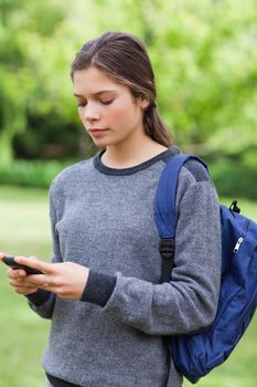 Young serious girl sending a text with her cellphone while standing in the countryside