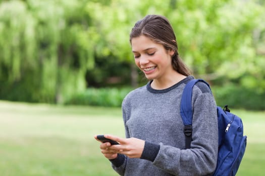 Smiling teenage girl receiving a text with her cellphone while standing in a park