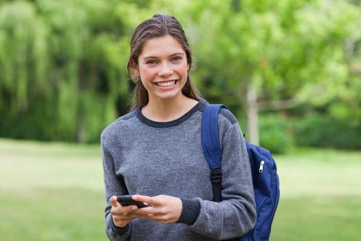Young smiling woman looking straight at the camera while using her mobile phone