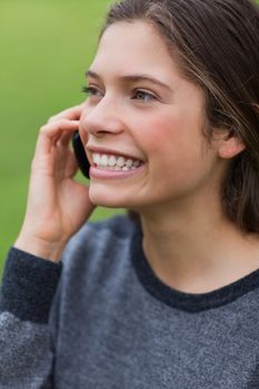 Young smiling girl using her mobile phone while standing upright in a park