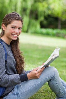 Young happy adult looking straight at the camera while beaming and reading a book