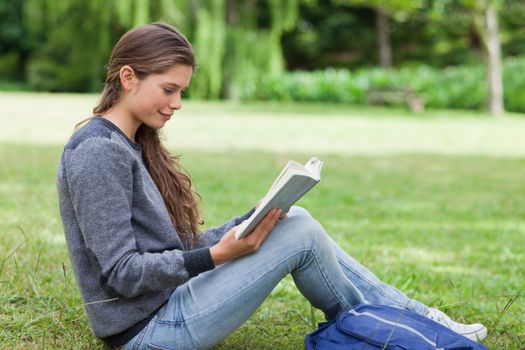 Young relaxed girl seriously reading a book while sitting on the grass in a park