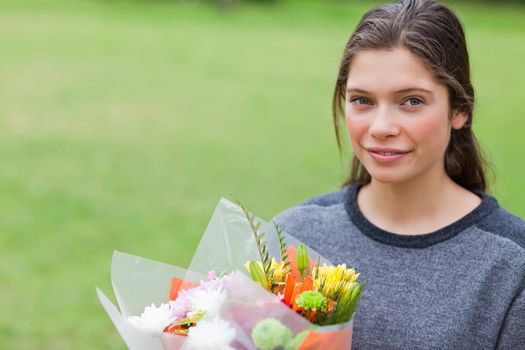 Calm teenager holding a beautiful bunch of flowers while standing up in a park