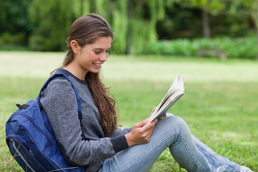 Young calm girl sitting on the grass while attentively reading a book