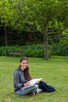Smiling teenage girl doing her homework while sitting on the grass in the countryside
