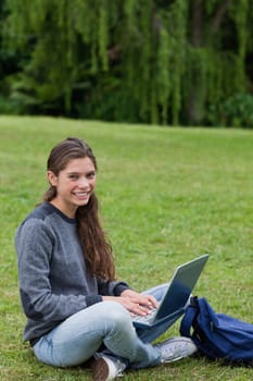 Student sitting cross-legged on the grass in the countryside while using her laptop
