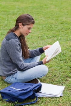 Young serious girl reading a book while sitting down with her notebook next to her