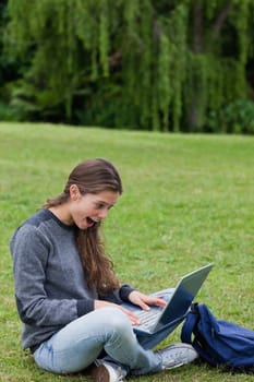 Young girl showing her surprise while looking at her laptop and sitting on the grass