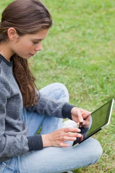 Young smiling girl sitting cross-legged on the grass while touching her tablet pc