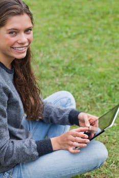 Young relaxed adult sitting down with her tablet computer while looking at the camera