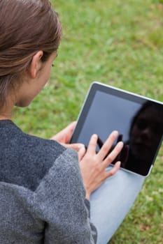 Rear view of a young girl using her tablet pc while sitting cross-legged in a park