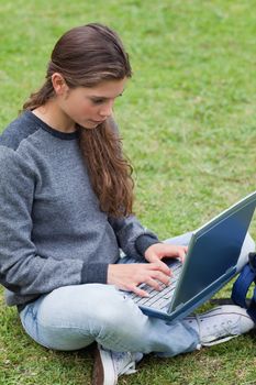 Serious young girl typing on her laptop while sitting cross-legged in a park
