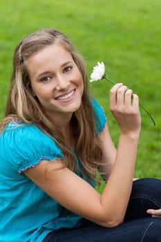 Young smiling woman holding a white flower while sitting down in the countryside