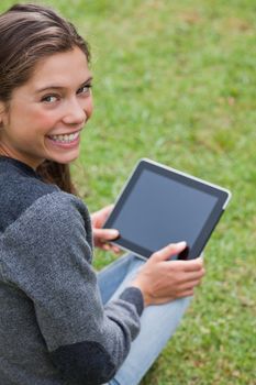 Young girl using her tablet computer while sitting on the grass and beaming