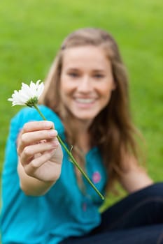 White flower held by a young smiling woman sitting in a park