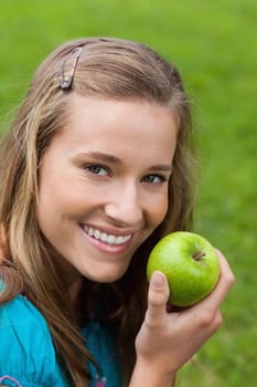 Attractive young girl eating a delicious green apple in the countryside