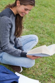 Young smiling woman holding a book while sitting down on the grass in a park