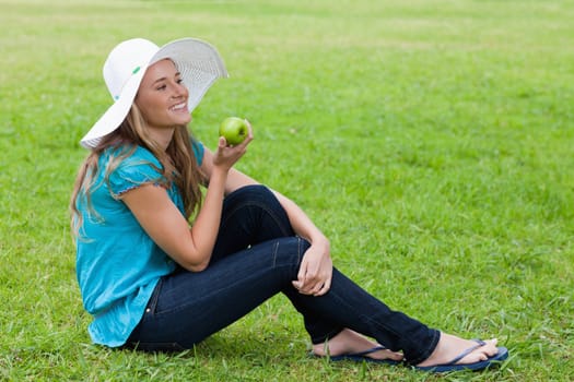 Young girl sitting cross-legged in a park while holding a green apple