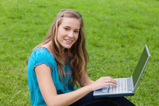 Young woman using her laptop in the countryside while looking straight at the camera