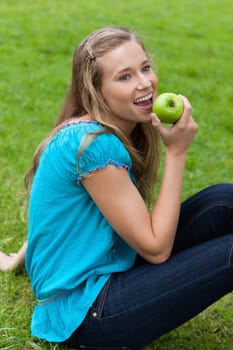 Smiling young girl eating a delicious green apple while looking towards the side