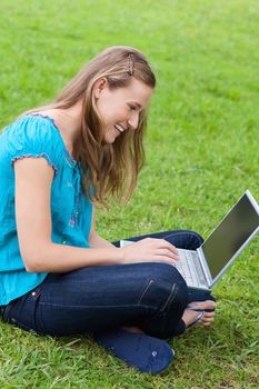 Young smiling woman sitting down in the countryside while typing on her laptop