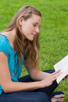 Young attractive girl sitting down on the grass in a park while reading a book