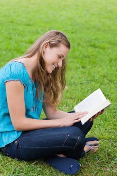 Happy young girl reading a book while sitting cross-legged on the grass in a park