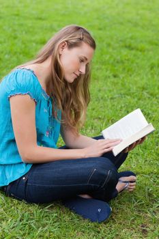 Serious young girl reading a book while sitting cross-legged in the countryside