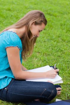 Young happy girl doing her homework while sitting on the grass in the countryside