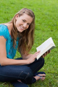 Young happy woman looking at the camera while reading a book in the countryside