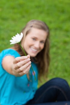 Beautiful white flower held by a young attractive girl sitting in the countryside