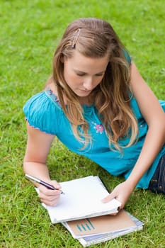 Serious student lying on the grass in the countryside while writing on a notebook