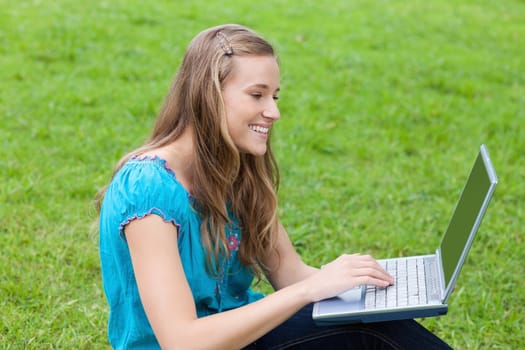 Young attractive girl looking at her laptop while sitting down on the grass in a park