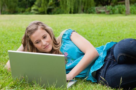 Calm student lying on the grass with her hand on head while working with her laptop