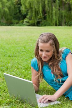 Smiling teenager lying on the grass in the countryside while typing on her laptop