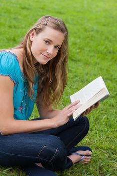 Young relaxed girl reading a book while sitting cross-legged on the grass in a park