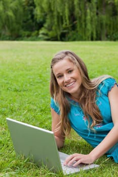 Young girl looking at the camera while typing on her laptop and showing a great smile