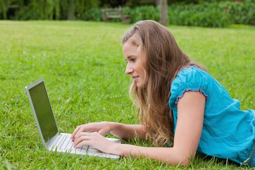 Side view of a young girl typing on her laptop while lying down in the countryside