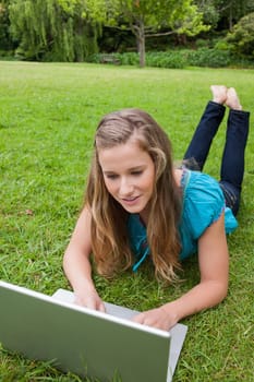 Young girl lying on the grass in the countryside with legs raised while using her laptop