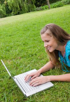 Smiling young woman lying in a public garden while attentively working on her laptop