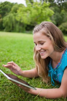 Young happy woman using her tablet pc while lying on the grass in a public garden