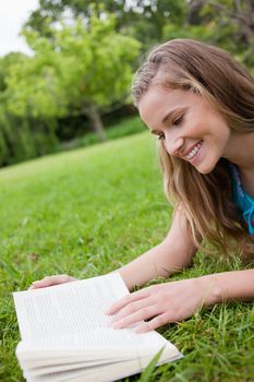 Young woman reading a book while lying on the grass in a parkland and smiling